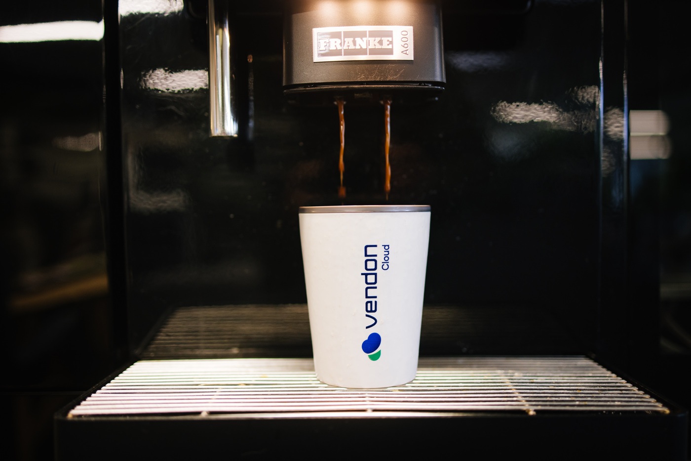 En kaffemaskine, der hælder espresso i en kop med Vendon Cloud-logo.